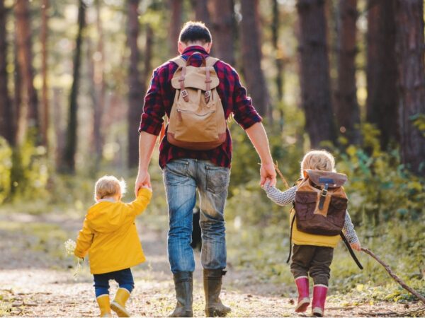 A father walking with two young children in a forest.
