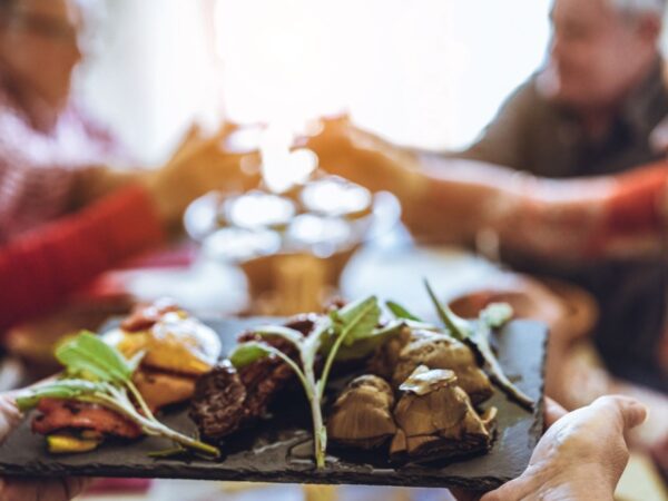 Chef bringing out platter of food, with group of people at a table in the background