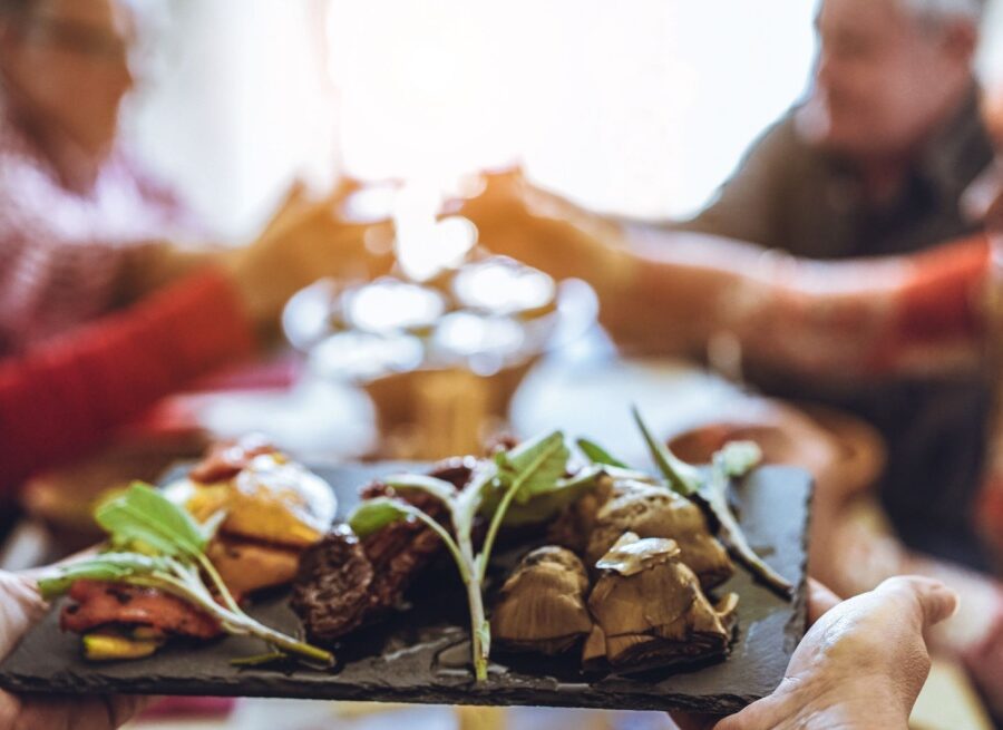 Chef bringing out platter of food, with group of people at a table in the background