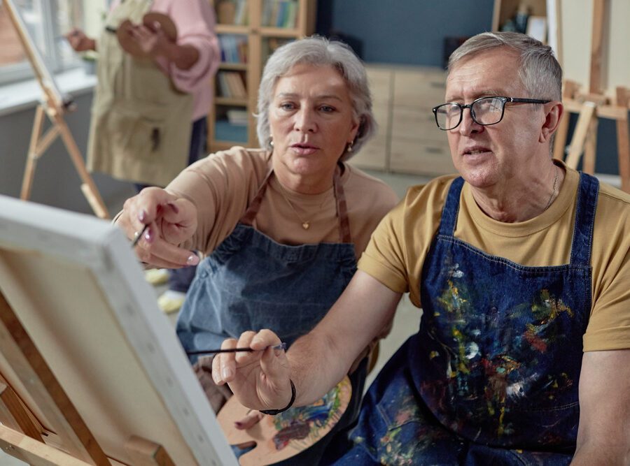 An older couple painting at an easel together.