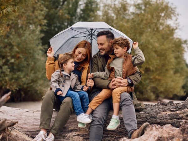 A young family sheltering under an umbrella and smiling