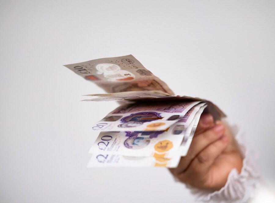 A hand holding UK bank notes.