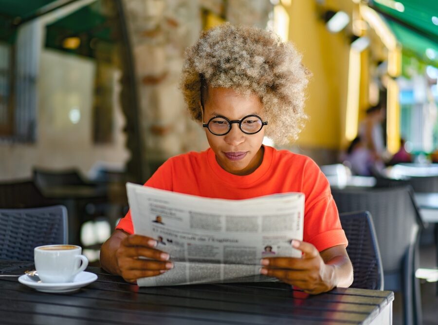 A woman reading a newspaper in a café.
