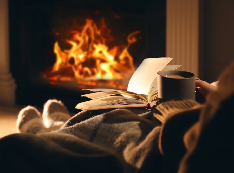 Person sitting with their feet up reading by an open fire